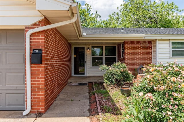 view of exterior entry with a garage, brick siding, and a shingled roof
