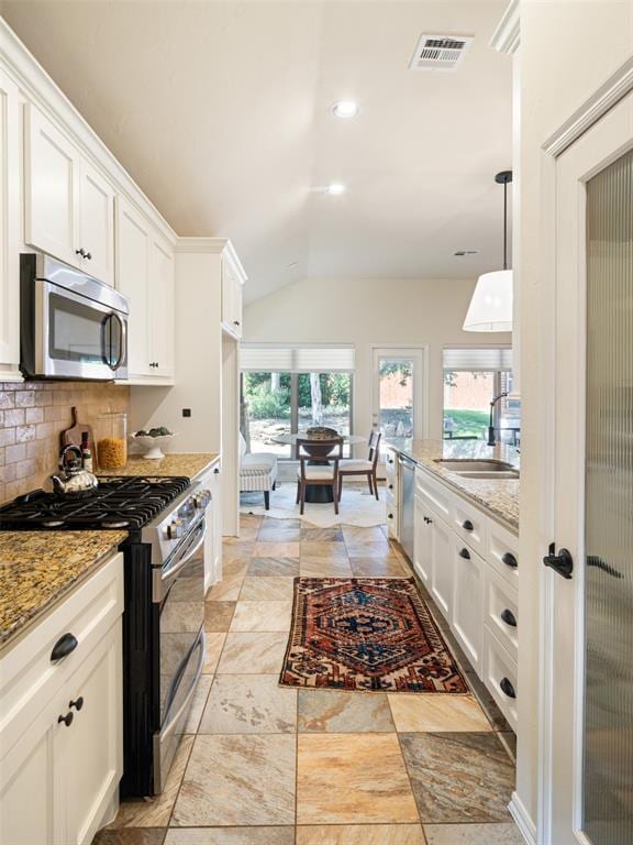 kitchen featuring stainless steel appliances, a sink, vaulted ceiling, white cabinets, and decorative backsplash