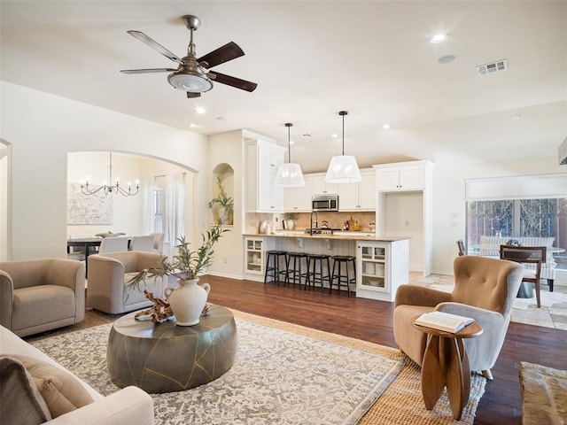 living area with arched walkways, dark wood-style flooring, a ceiling fan, recessed lighting, and a chandelier