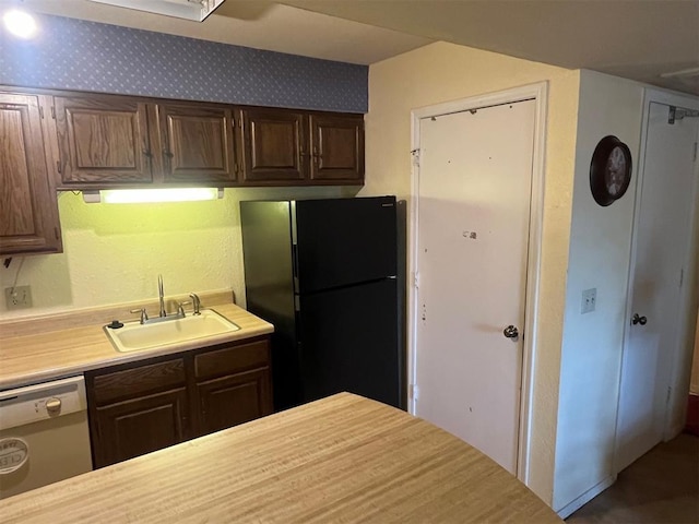 kitchen featuring freestanding refrigerator, a sink, dishwashing machine, light countertops, and dark brown cabinets