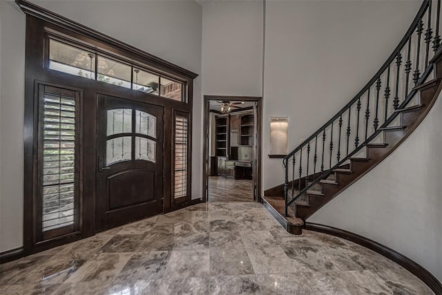 foyer entrance with a high ceiling, stairs, ceiling fan, baseboards, and marble finish flooring