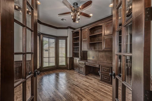 unfurnished office with french doors, built in desk, dark wood finished floors, a ceiling fan, and crown molding