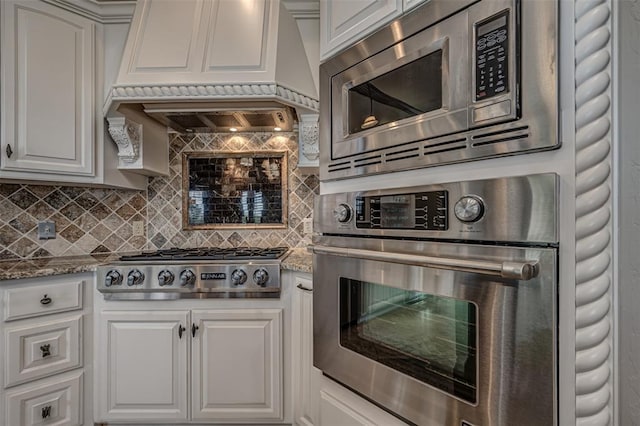 kitchen featuring stainless steel appliances, custom range hood, tasteful backsplash, light stone counters, and white cabinets