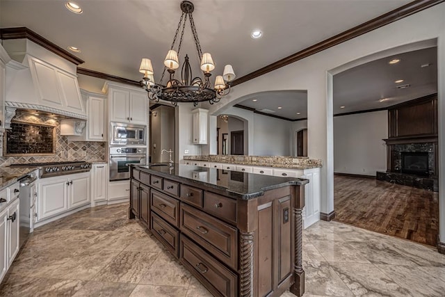 kitchen featuring stainless steel appliances, crown molding, arched walkways, white cabinetry, and decorative backsplash