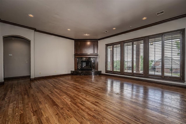 unfurnished living room with ornamental molding, arched walkways, wood finished floors, a premium fireplace, and baseboards