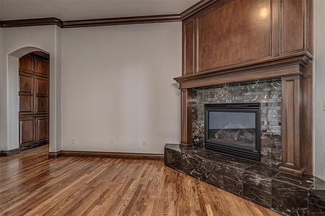 unfurnished living room featuring crown molding, wood finished floors, baseboards, arched walkways, and a high end fireplace