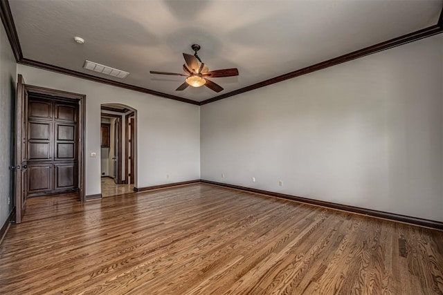 spare room featuring ceiling fan, wood finished floors, arched walkways, baseboards, and ornamental molding
