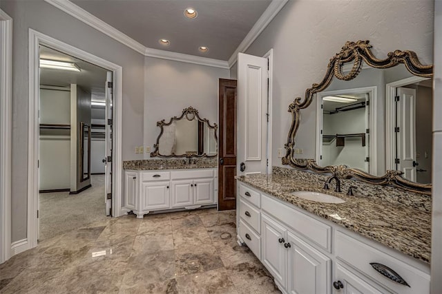 bathroom featuring crown molding, two vanities, a walk in closet, and recessed lighting