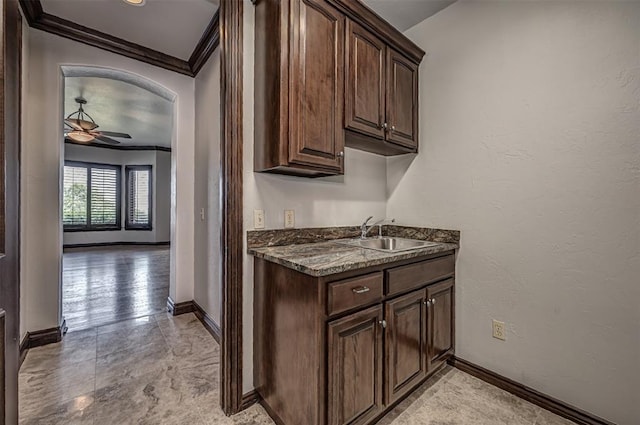 kitchen with a sink, ornamental molding, dark brown cabinetry, baseboards, and arched walkways
