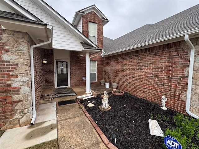 view of exterior entry featuring roof with shingles, brick siding, and stone siding