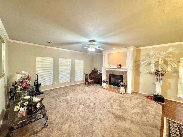living room featuring a ceiling fan, a tile fireplace, carpet, baseboards, and ornamental molding