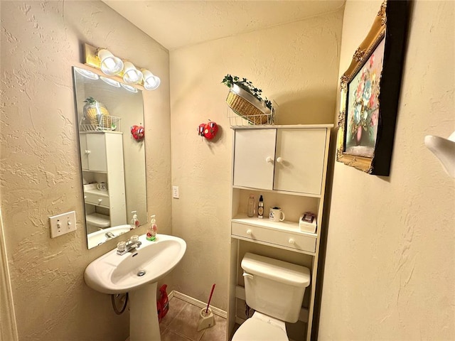 bathroom with tile patterned floors, toilet, a textured wall, a sink, and baseboards