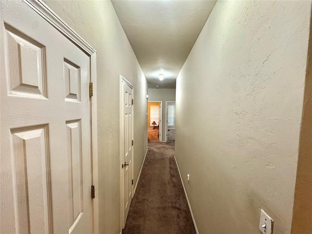 hallway featuring dark colored carpet and baseboards