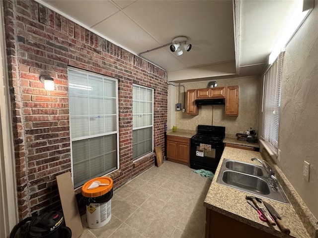 kitchen with black range with gas cooktop, a sink, under cabinet range hood, light countertops, and brown cabinetry