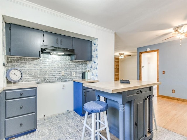 3208 NW 34th St, Oklahoma City, OK 73112 - kitchen with ceiling fan, under cabinet range hood, decorative backsplash, a kitchen breakfast bar, and crown molding