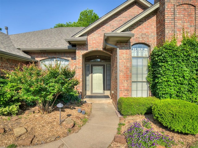 entrance to property featuring brick siding and a shingled roof
