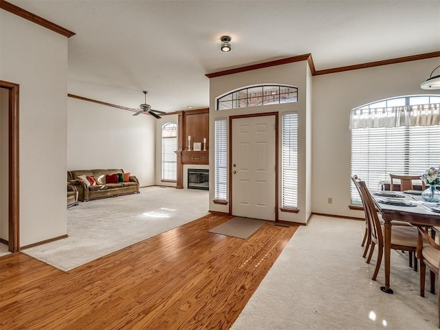 foyer entrance with light carpet, ornamental molding, a fireplace, baseboards, and a ceiling fan