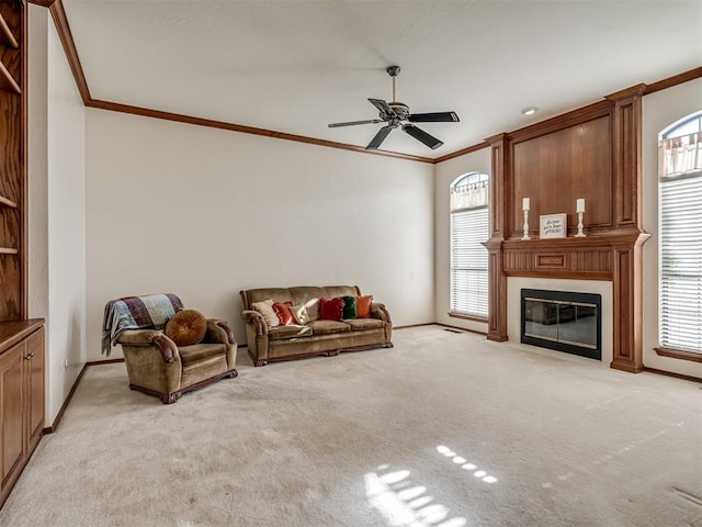 living room featuring ornamental molding, plenty of natural light, a ceiling fan, a fireplace, and baseboards