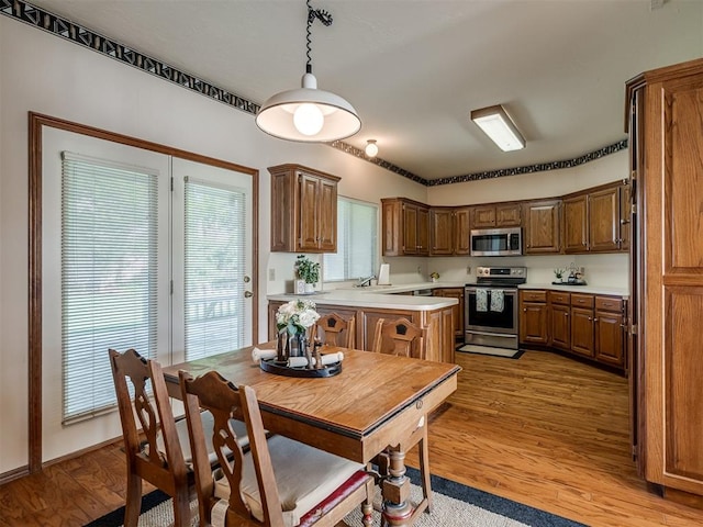kitchen featuring appliances with stainless steel finishes, light countertops, light wood-style floors, decorative light fixtures, and brown cabinets