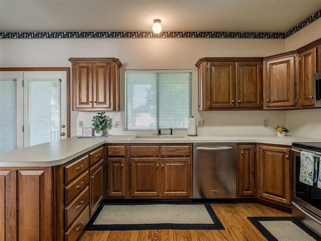 kitchen featuring stainless steel appliances, a sink, a peninsula, wood finished floors, and light countertops
