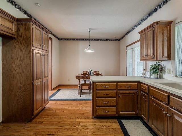 kitchen featuring light wood-style flooring, a peninsula, light countertops, hanging light fixtures, and a sink