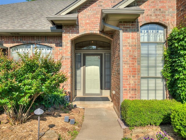 doorway to property featuring brick siding and a shingled roof