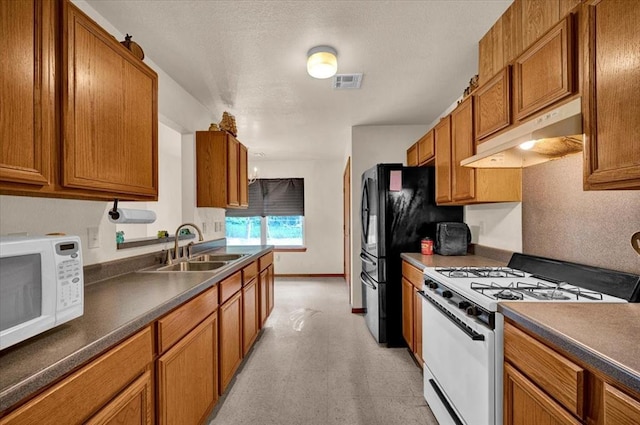 kitchen featuring white appliances, a sink, under cabinet range hood, brown cabinetry, and dark countertops