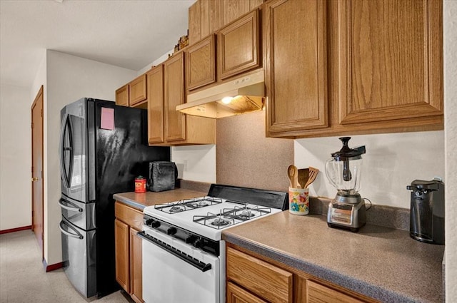 kitchen with white gas range, under cabinet range hood, freestanding refrigerator, brown cabinets, and baseboards