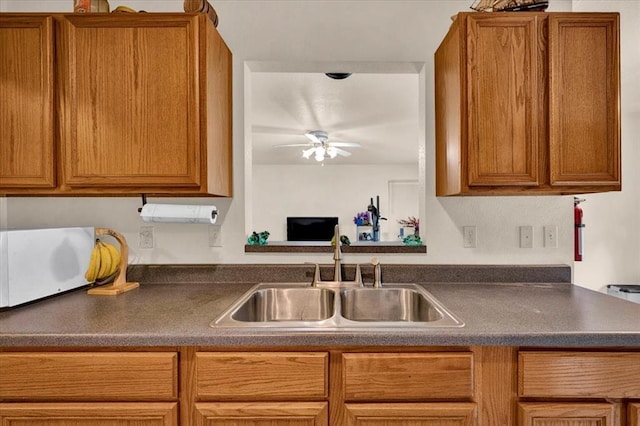 kitchen with a sink, dark countertops, a ceiling fan, and brown cabinetry
