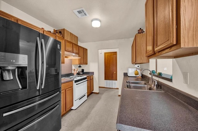 kitchen featuring white appliances, a sink, light flooring, dark countertops, and brown cabinets
