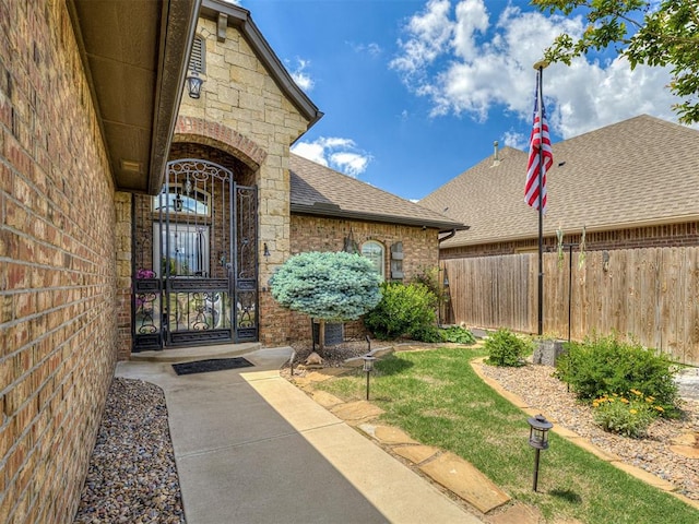 entrance to property with fence, brick siding, a shingled roof, and stone siding