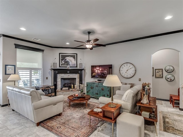 living room with ornamental molding, arched walkways, a ceiling fan, a fireplace with raised hearth, and recessed lighting