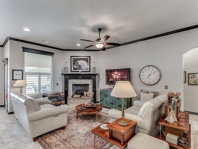 living area with ornamental molding, ceiling fan, arched walkways, a fireplace with raised hearth, and recessed lighting