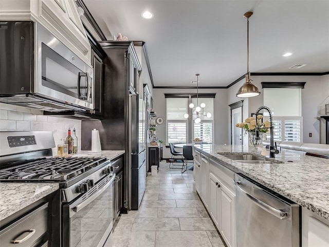 kitchen featuring appliances with stainless steel finishes, a sink, ornamental molding, backsplash, and light stone counters
