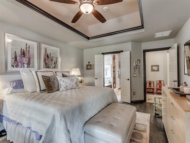 bedroom with a raised ceiling, dark wood-style flooring, and a ceiling fan