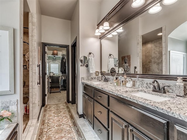 bathroom with a tile shower, a walk in closet, and double vanity