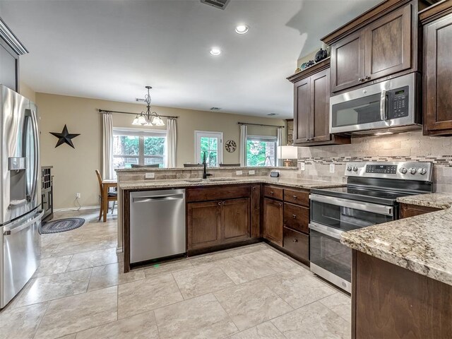 3570 Riverwood Ln, Edmond, OK 73034 - kitchen with appliances with stainless steel finishes, a sink, a peninsula, dark brown cabinetry, and light stone countertops