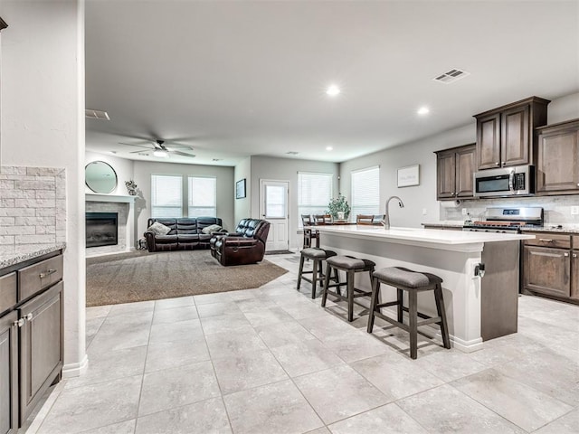 10301 NW 25th St, Yukon, OK 73099 - kitchen featuring appliances with stainless steel finishes, a breakfast bar, light countertops, a kitchen island with sink, and a ceiling fan