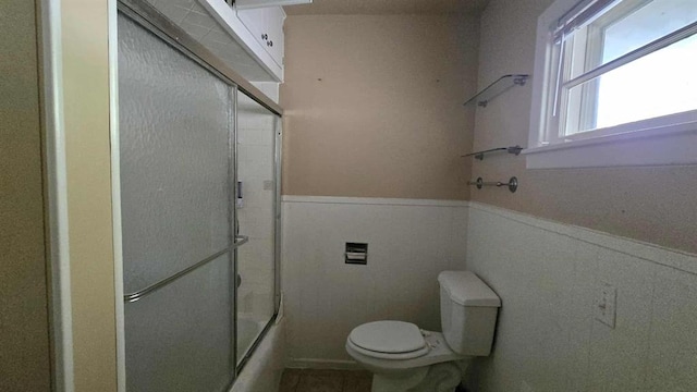 full bath featuring a wainscoted wall, toilet, and bath / shower combo with glass door