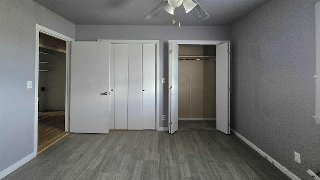 unfurnished bedroom with wood finished floors, baseboards, two closets, and ceiling fan