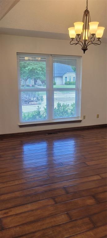 unfurnished room featuring healthy amount of natural light, a chandelier, and dark wood-style flooring