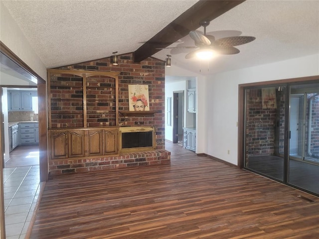 unfurnished living room featuring a ceiling fan, a textured ceiling, dark wood-type flooring, a fireplace, and baseboards