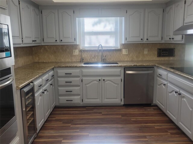 kitchen featuring stainless steel appliances, a sink, beverage cooler, under cabinet range hood, and white cabinetry