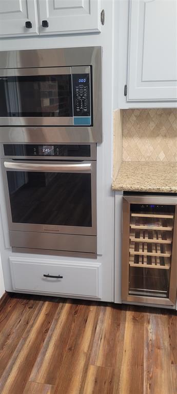 kitchen view of appliances with stainless steel finishes, beverage cooler, white cabinetry, backsplash, and light stone countertops
