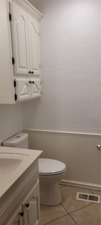 bathroom with toilet, tile patterned floors, vanity, a decorative wall, and wainscoting