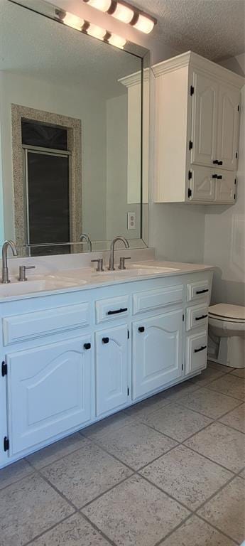 bathroom with double vanity, toilet, and a textured ceiling