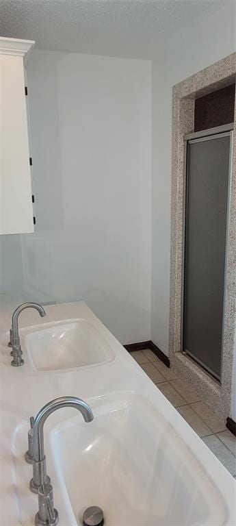 full bathroom with a sink, a stall shower, a textured ceiling, and tile patterned flooring