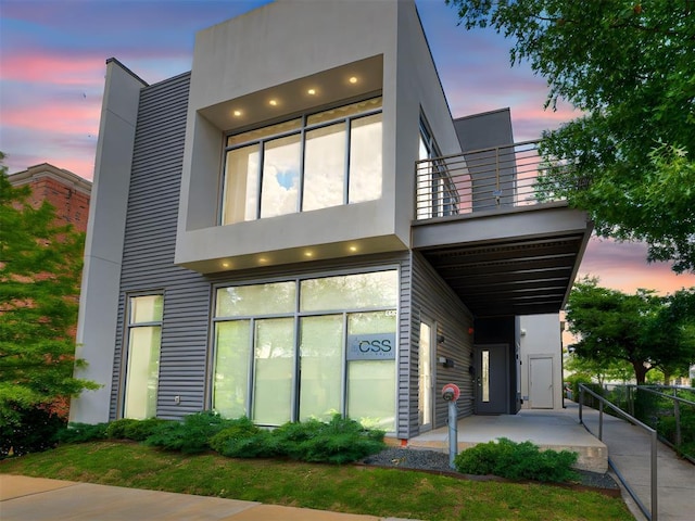 view of front of property featuring a balcony, stucco siding, and fence