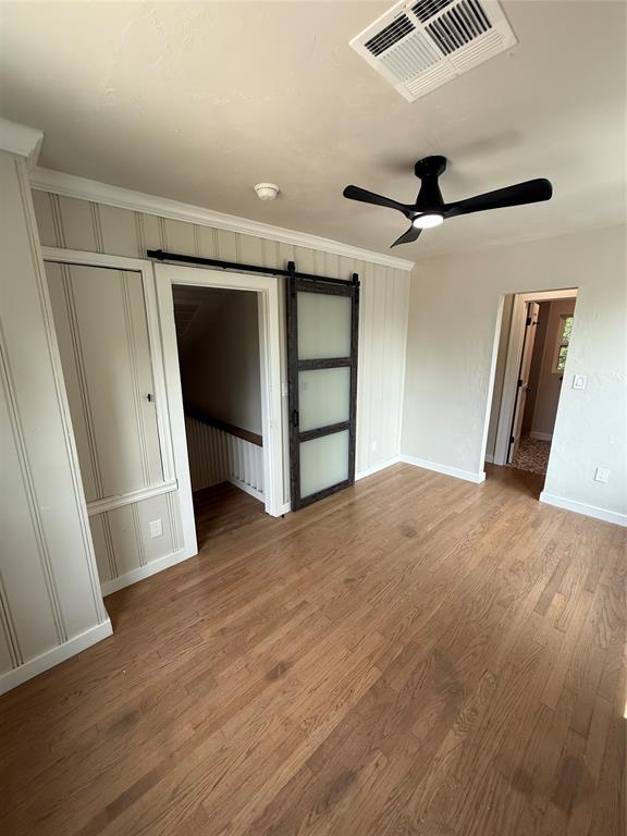 1212 NW 48th St, Oklahoma City, OK 73118 - unfurnished bedroom featuring a barn door, wood finished floors, baseboards, crown molding, and ceiling fan