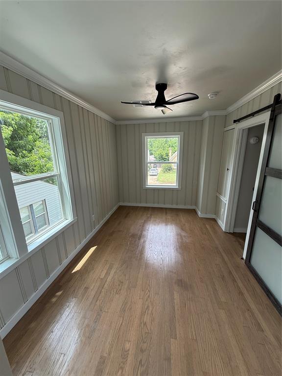 1212 NW 48th St, Oklahoma City, OK 73118 - spare room featuring a barn door, wood finished floors, crown molding, a ceiling fan, and a decorative wall